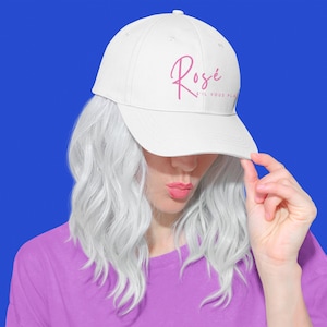 May include: White baseball cap with the word "Rose" written in pink cursive on the front. The text below "Rose" says "s'il vous plait".