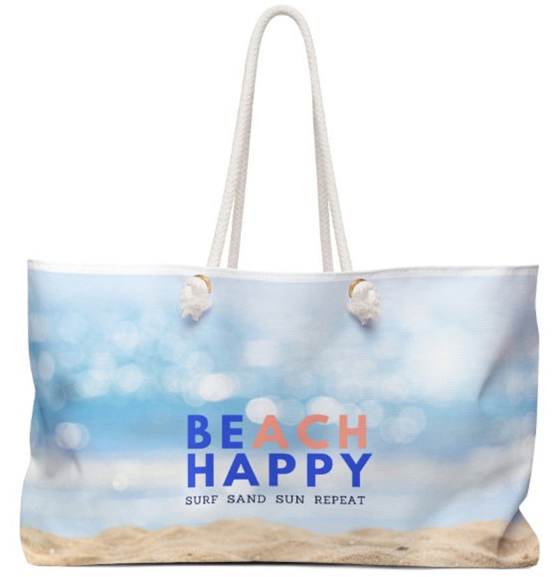 May include: White canvas tote bag with a blue and white beach scene and the text "Beach Happy Surf Sand Sun Repeat".