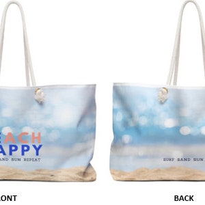 May include: A white canvas tote bag with a beach scene and the text "BEACH HAPPY" in blue and pink. The text "SURF SAND SUN REPEAT" is printed in blue on the front of the bag. The back of the bag has the text "SURF SAND SUN REPEAT" printed in blue.