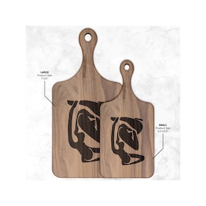 Może przedstawiać: Dwie drewniane deski do krojenia z uchwytami, jedna duża (17,8 cm x 38,1 cm) i jedna mała (14 cm x 29,2 cm). Każda deska ma czarny abstrakcyjny wzór. Deski są wykonane z jasnobrązowego drewna.
