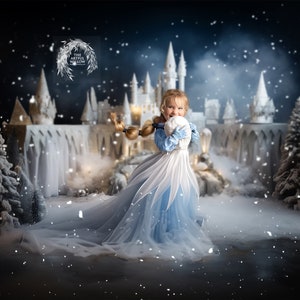May include: A young girl dressed in a blue and white princess costume holds a snowball in front of a snowy castle backdrop. The castle is decorated with lights and there are snow-covered trees in the foreground.
