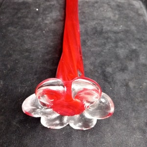 May include: A red glass vase with a swirl design and a clear glass flower-shaped base.