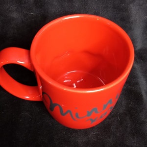 May include: Red ceramic mug with a black cursive inscription that reads "Minnie Mouse".