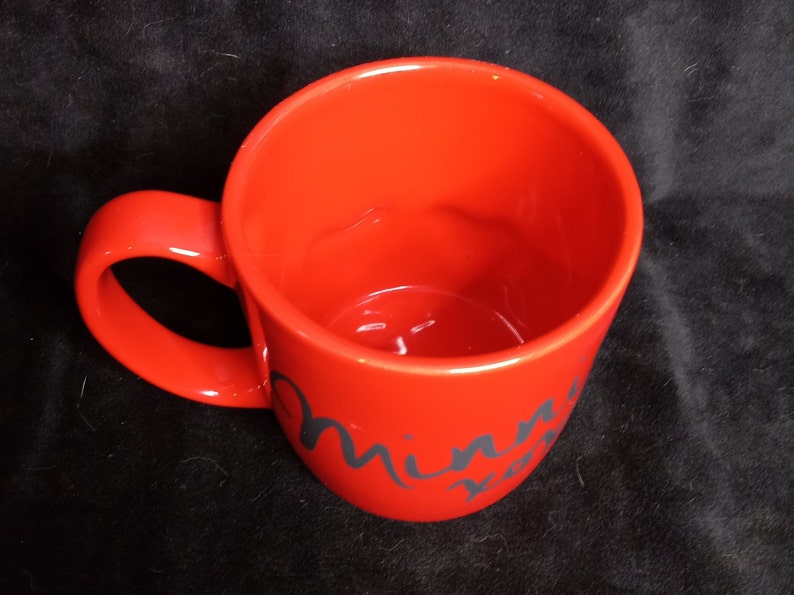 May include: Red ceramic mug with a black cursive inscription that reads "Minnie Mouse".