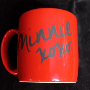 May include: Red ceramic mug with a black handwritten inscription that says "Minnie xoxo".