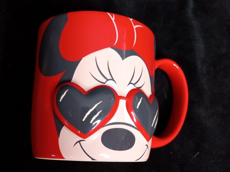 May include: Red ceramic mug with a cartoon image of Minnie Mouse wearing heart-shaped sunglasses.
