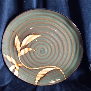 May include: A brown and green ceramic dinner plate with a swirling pattern and a gold leaf design.