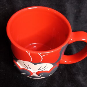 May include: Red ceramic mug with a black and white image of Minnie Mouse wearing sunglasses. The mug has a black handle.