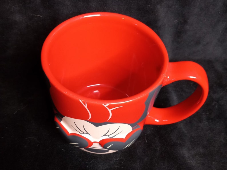 May include: Red ceramic mug with a black and white image of Minnie Mouse wearing sunglasses. The mug has a black handle.