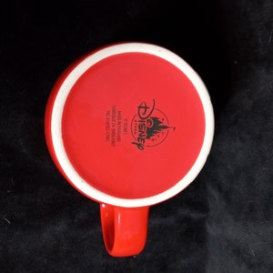 May include: Red ceramic mug with a white rim and a black Disney Store logo on the bottom. The logo includes the words "Disney Store" and "Made in Thailand".