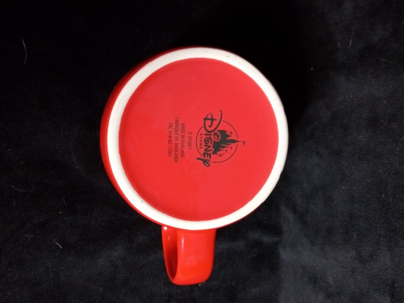 May include: Red ceramic mug with a white rim and a black Disney Store logo on the bottom. The logo includes the words "Disney Store" and "Made in Thailand".