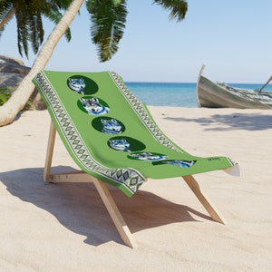 Puede incluir: Una silla de playa verde con un diseño de lobo. La silla tiene un fondo verde con un patrón de diamantes negros y blancos. El diseño del lobo está en un círculo con un fondo negro. La silla está en una playa de arena.