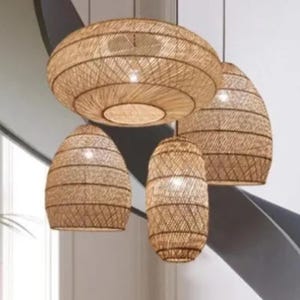 May include: A set of four woven pendant lights, featuring a large, round, flat shade and three smaller, oval shades. The lights are made of natural, light brown woven material and are hanging from a ceiling.