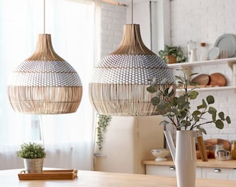 May include: Two white and brown woven pendant lights hang over a wooden table with white chairs. The lights are in a kitchen setting with white cabinets and a white brick wall.