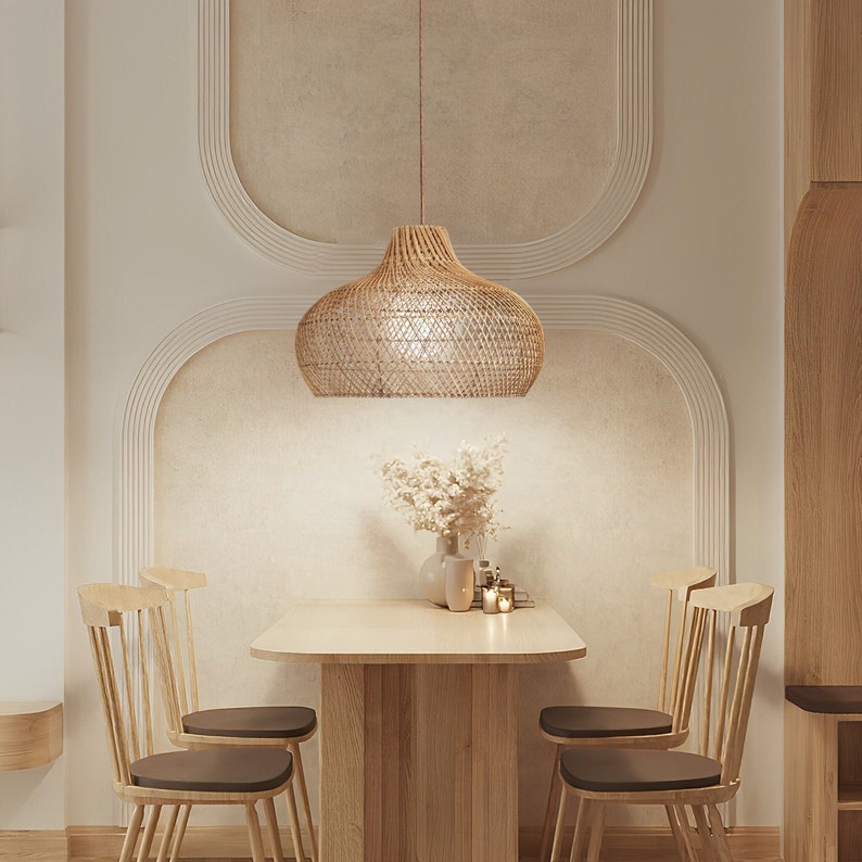 May include: A woven rattan pendant light hangs over a wooden dining table with four chairs. The table is set with a vase of dried flowers and candles.