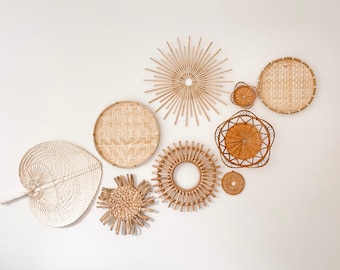 May include: A collection of nine woven wall decor pieces in various shapes and sizes, including a large fan-shaped piece, round and starburst shapes, and a few smaller round pieces. The pieces are made of natural materials and have a light brown color.