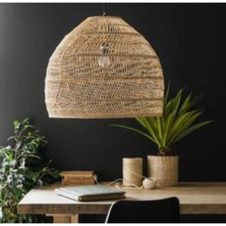 May include: A woven natural fiber pendant light fixture with a dome shape hangs from the ceiling over a table with plants and books.