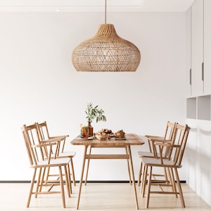 May include: A woven rattan pendant light hangs over a wooden dining table with four chairs. The table is set with a bowl of fruit and a plate of pastries.