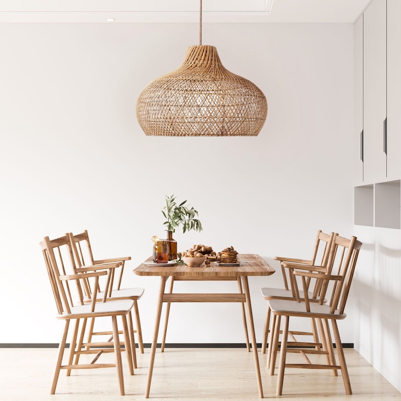 May include: A woven rattan pendant light hangs over a wooden dining table with four chairs. The table is set with a bowl of fruit and a plate of pastries.