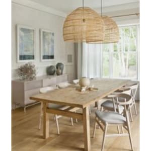 May include: A light wood dining table with six chairs. The table has a natural wood finish and the chairs are white with a woven seat. Two woven wicker pendant lights hang above the table.
