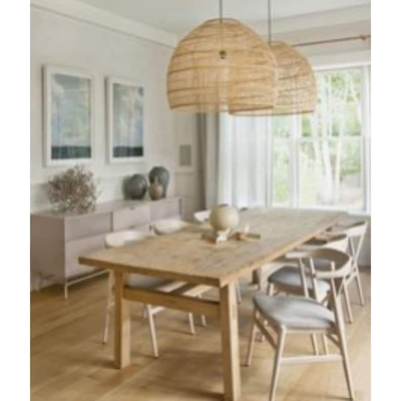 May include: A light wood dining table with six chairs. The table has a natural wood finish and the chairs are white with a woven seat. Two woven wicker pendant lights hang above the table.