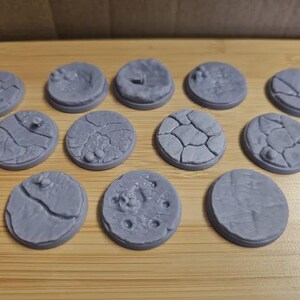 Peut inclure: Une collection de socles miniatures circulaires gris avec des surfaces texturées. Les socles présentent divers motifs, notamment de la terre craquelée, des surfaces lisses et de petits détails, adaptés aux jeux de société.