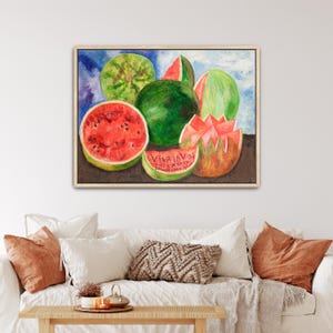 May include: Watercolor painting of watermelons in various forms: whole, sliced, and carved. The painting features vibrant red and green hues, with the text "VIVA LA VIDA" on a watermelon slice. The artwork is framed in a light wood frame.