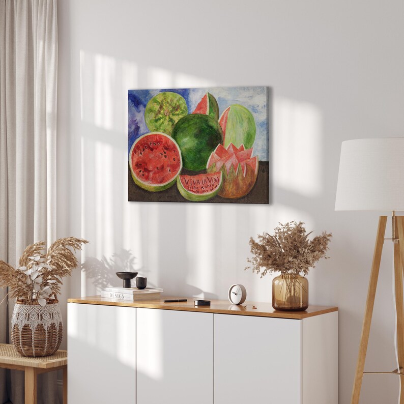 May include: A watercolor painting of watermelons. The painting features whole and sliced watermelons in shades of green and red against a blue and white background. The painting is displayed on a white wall.