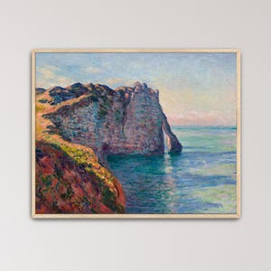 May include: A framed oil painting depicting a coastal landscape with a large, textured cliff face extending into a calm sea. The scene features vibrant brushstrokes in shades of blue, green, orange, and yellow, capturing the light on the rock.