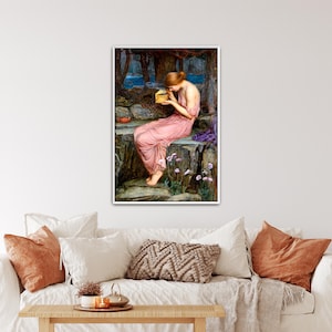 May include: A framed print of a classical painting. A woman in a pink dress sits on a stone wall, holding a small golden box. The background features a forest and a body of water. The artwork is displayed above a white couch with orange and white pillows.