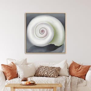 May include: A square wall art print featuring a large, white, spiral seashell centred against a dark grey background. The shell displays a smooth, curved surface with a soft pinkish-tan centre and a subtle pale green tint along its outer edge.