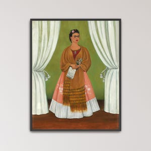 May include: A framed print of a woman in a traditional dress, holding flowers and a paper. The woman wears a brown shawl over a red top and a long pink skirt. She has a flower in her hair and stands in front of green and white curtains.