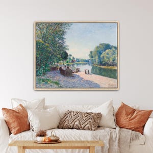 Può includere: Un dipinto paesaggistico incorniciato che raffigura una scena fluviale con alberi verdi rigogliosi, una riva sabbiosa e piccole figure vicino a una struttura. L'opera presenta un cielo azzurro e morbide pennellate impressioniste nei toni del verde.