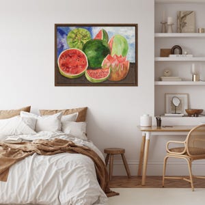 May include: Watercolor painting of watermelons in various forms: whole, sliced, and cut. The painting features vibrant red and green hues, with the text "VIVA LA VIDA" visible on one slice. The artwork is framed in a dark brown wooden frame.
