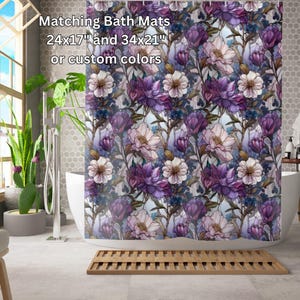 May include: A shower curtain with a floral pattern featuring purple and white flowers. The text "Matching Bath Mats 24x17" and 34x21" or custom colors" is printed at the top of the curtain.