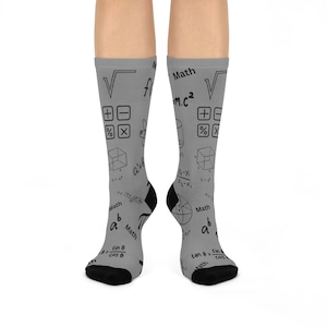 May include: A pair of grey socks with a black and white mathematical pattern. The socks feature various mathematical symbols, equations, and formulas, including pi, square roots, and the Pythagorean theorem. The socks are a fun and quirky way to show your love of maths.