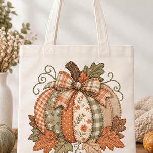 May include: A white canvas tote bag featuring a central graphic of a pumpkin composed of various fabric patches in shades of orange, green, and beige. The pumpkin is decorated with a plaid bow and surrounded by embroidered autumn leaves and vines.