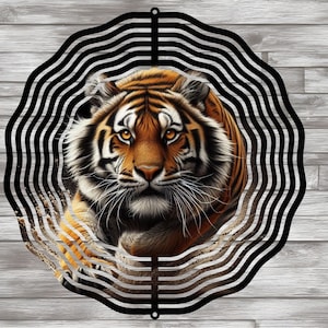 Könnte beinhalten: Ein schwarzer Windfänger aus Metall mit einem Tigergesichtsdesign. Der Tiger hat orange und schwarze Streifen auf weißem Hintergrund. Der Windfänger hat eine runde Form mit mehreren Metallschichten.