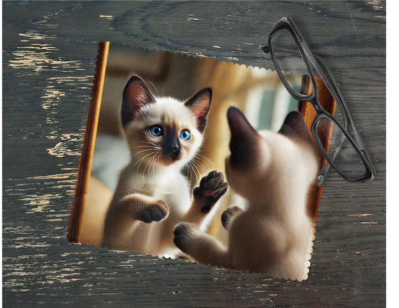 This adorable Siamese kitten looking at himself in a mirror microfiber lens cleaning cloth features a cute kitten design, perfect for cleaning glasses, camera lenses, phone screens, and other surfaces.