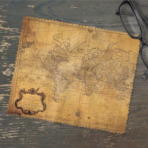 May include: An antique-style world map with intricate details and a decorative border. The map is printed on aged paper, featuring a compass rose and text in a decorative frame. Black-framed eyeglasses rest on a wooden surface.