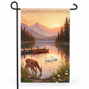 May include: A rectangular garden flag featuring a scenic landscape with a lake, mountains, and pine trees at sunset. A wooden dock and canoe sit on the water, while a deer and fawn drink from the shore near two white swans and colorful wildflowers.
