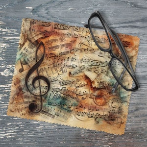 May include: A microfiber cleaning cloth with a vintage music sheet design featuring a treble clef and musical notes. The cloth is brown, beige, and blue with a faded look. A pair of black eyeglasses is lying on top of the cloth.