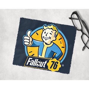 May include: A navy blue Fallout 76 microfiber cleaning cloth featuring the Vault Boy character giving a thumbs up. The cloth has a scalloped edge and the text "Fallout 76" in white and yellow.