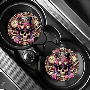 Puede incluir: Dos posavasos redondos para coche con un diseño de calavera steampunk. La calavera lleva un sombrero de copa con engranajes y ruedas dentadas. El fondo es una mezcla de dorado, negro y rosa.