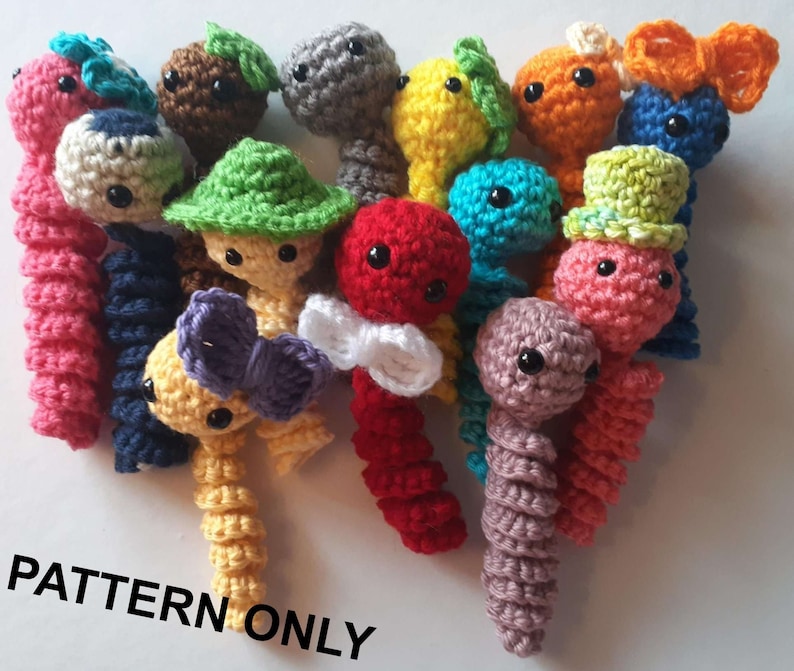May include: A collection of colourful crocheted amigurumi worm toys. Each worm has a unique personality with different hats, bows, and facial expressions. The text "PATTERN ONLY" is visible at the bottom of the image.