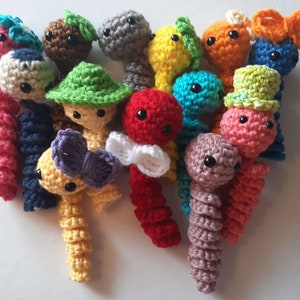 May include: A collection of colourful crocheted worm toys. The worms are made in a variety of colours, including pink, red, yellow, blue, green, brown, and grey. Some of the worms have hats or bows.