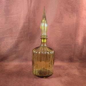 May include: A vintage amber glass bottle with a ribbed design and a tall, pointed stopper. The bottle has a rounded base and a slender neck, with a yellow-tinted stopper. The overall design is elegant and decorative.