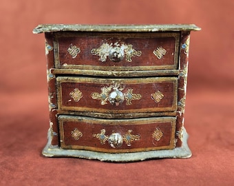 May include: A small wooden chest with three drawers. The drawers are painted red with gold accents and have decorative metal knobs. The chest is in a distressed vintage style.