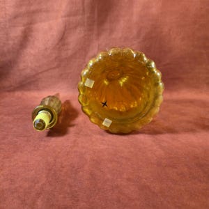 May include: An amber-colored glass perfume bottle with a matching stopper. The bottle has a round, ribbed body and a scalloped rim. The stopper is long and slender, with a rounded top and a yellow base.