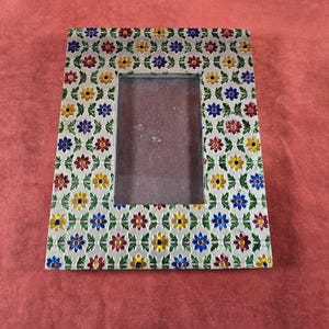 May include: A silver picture frame with a floral design in shades of red, yellow, blue, and green. The frame has a clear glass insert.